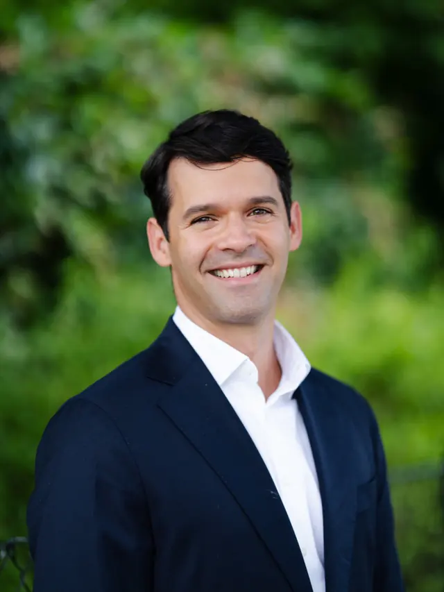 André Hartmann smiler i mørk dress og hvit skjorte.